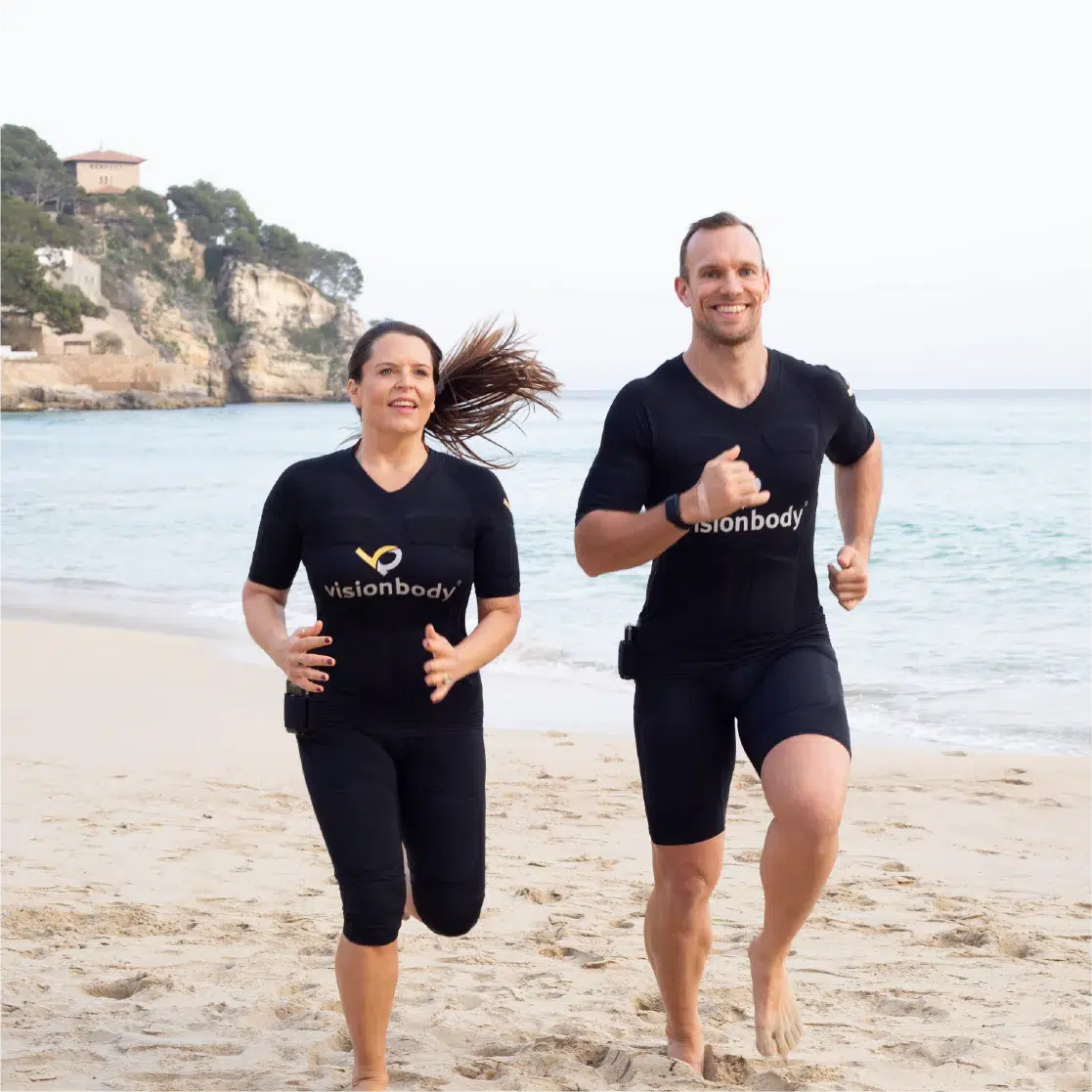 Two people jogging on the beach wearing black WB-EMS sportswear.