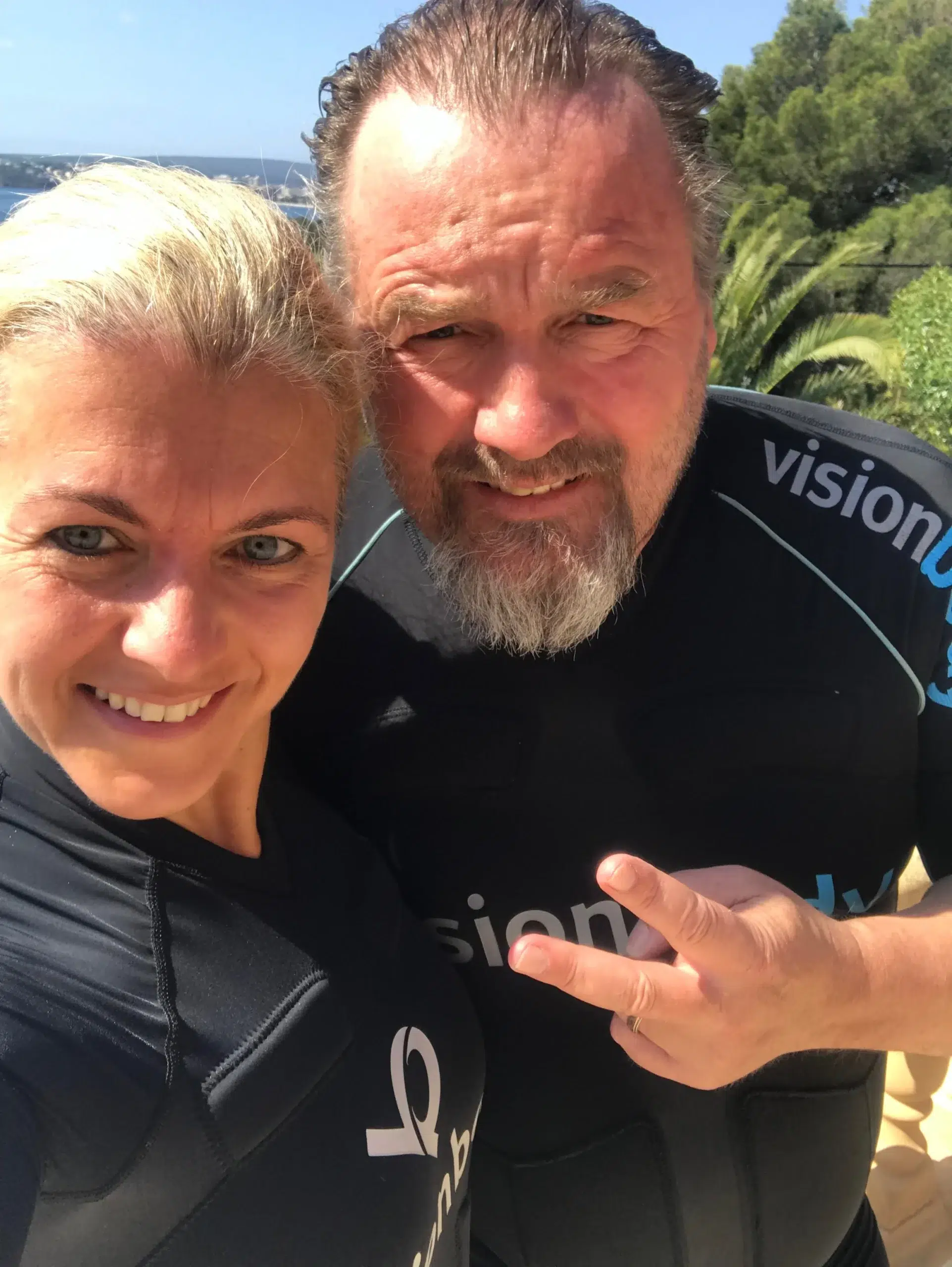 Two people in wetsuits, posing for a selfie outdoors.